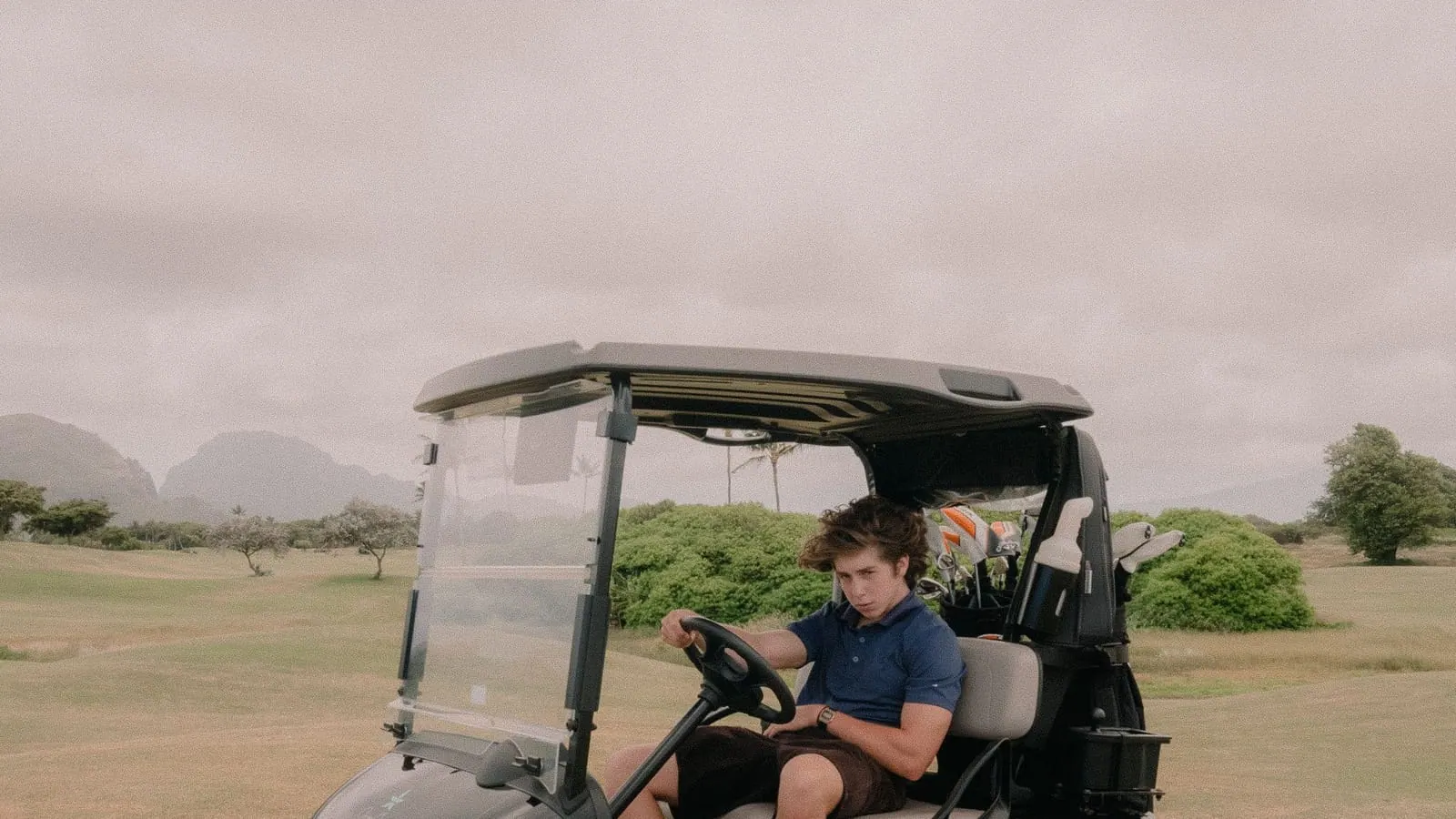 A driver at the wheel of a black electric golf cart crossing an open course