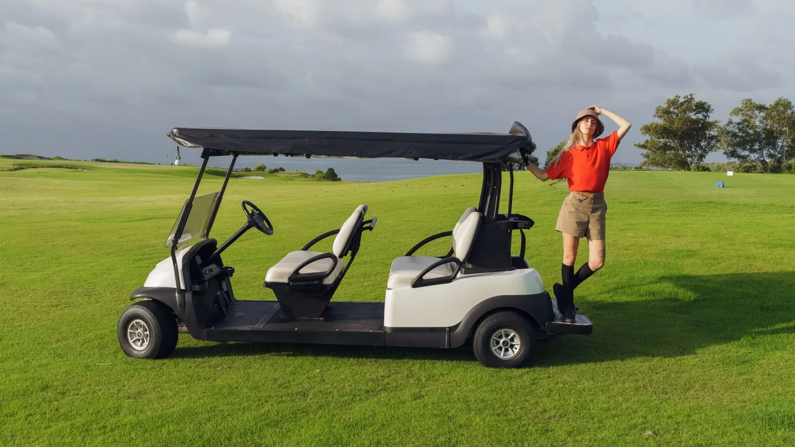 A white four-passenger electric golf cart on open grass in late afternoon light