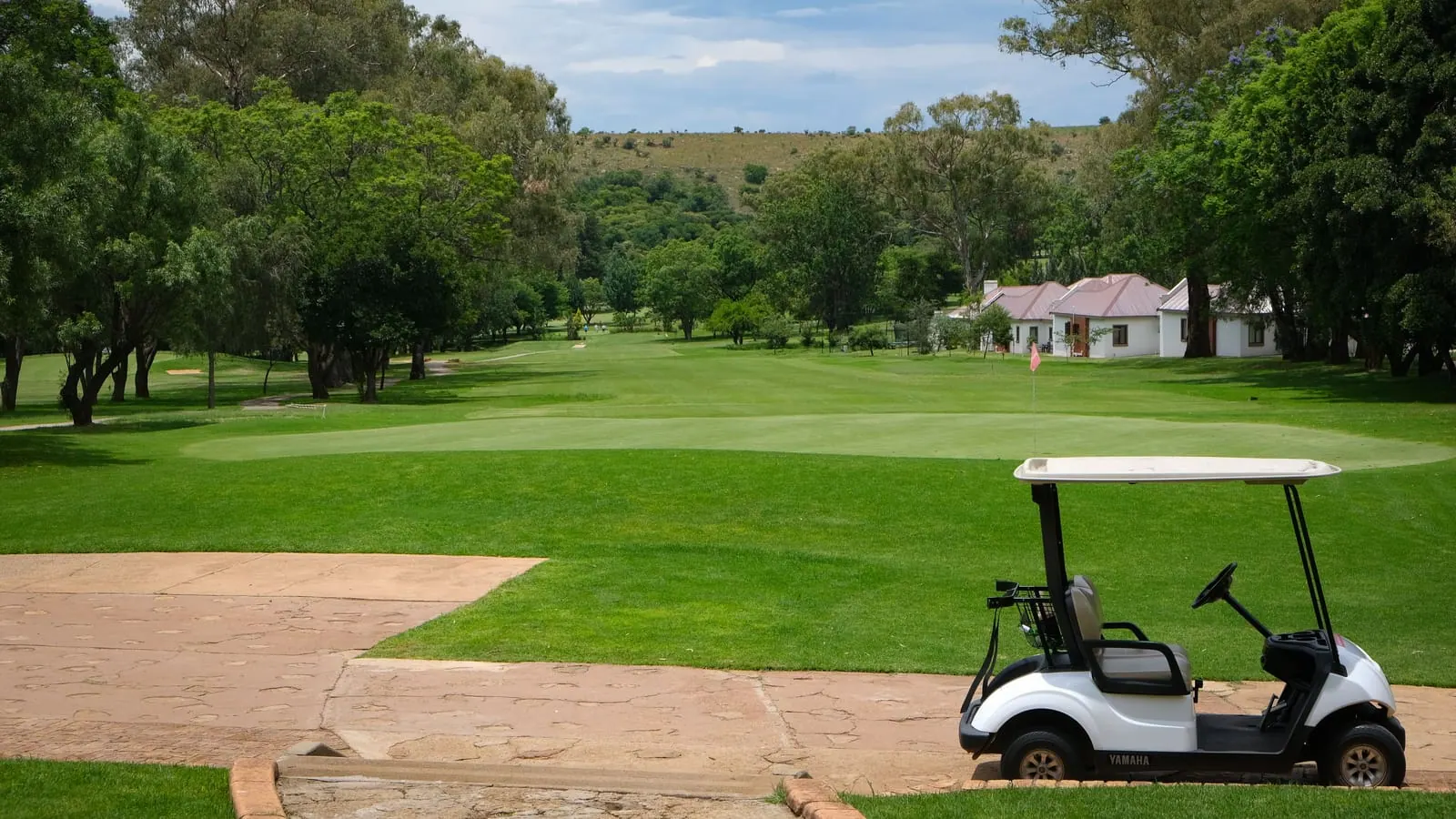 A white golf cart parked at the edge of a fairway with a clubhouse in the distance