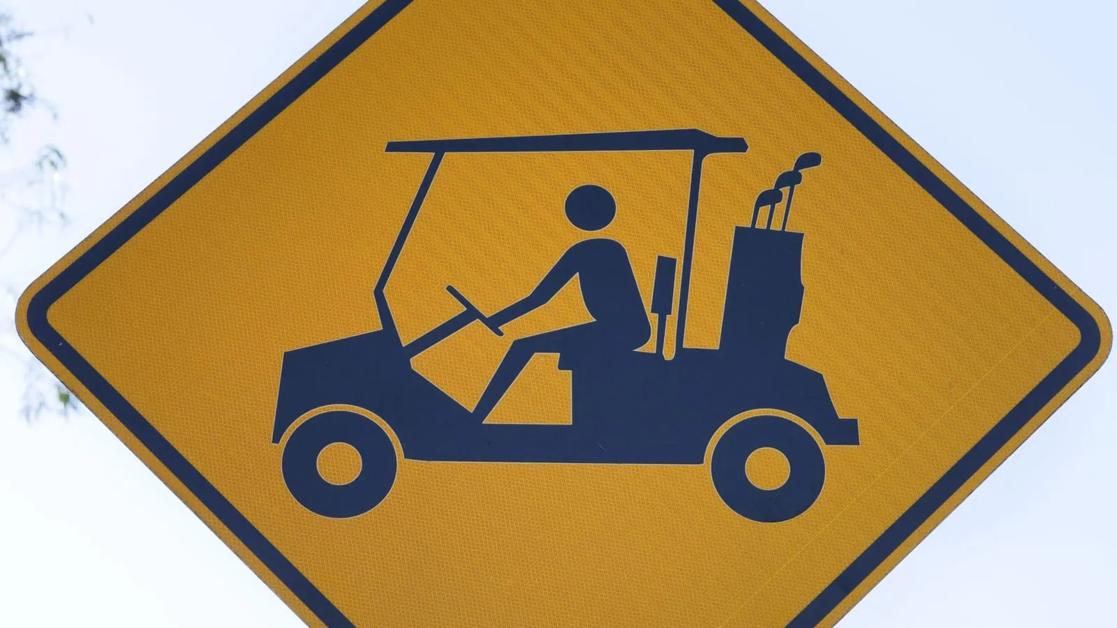 A yellow diamond road sign showing a golf cart symbol above a plate reading ONLY