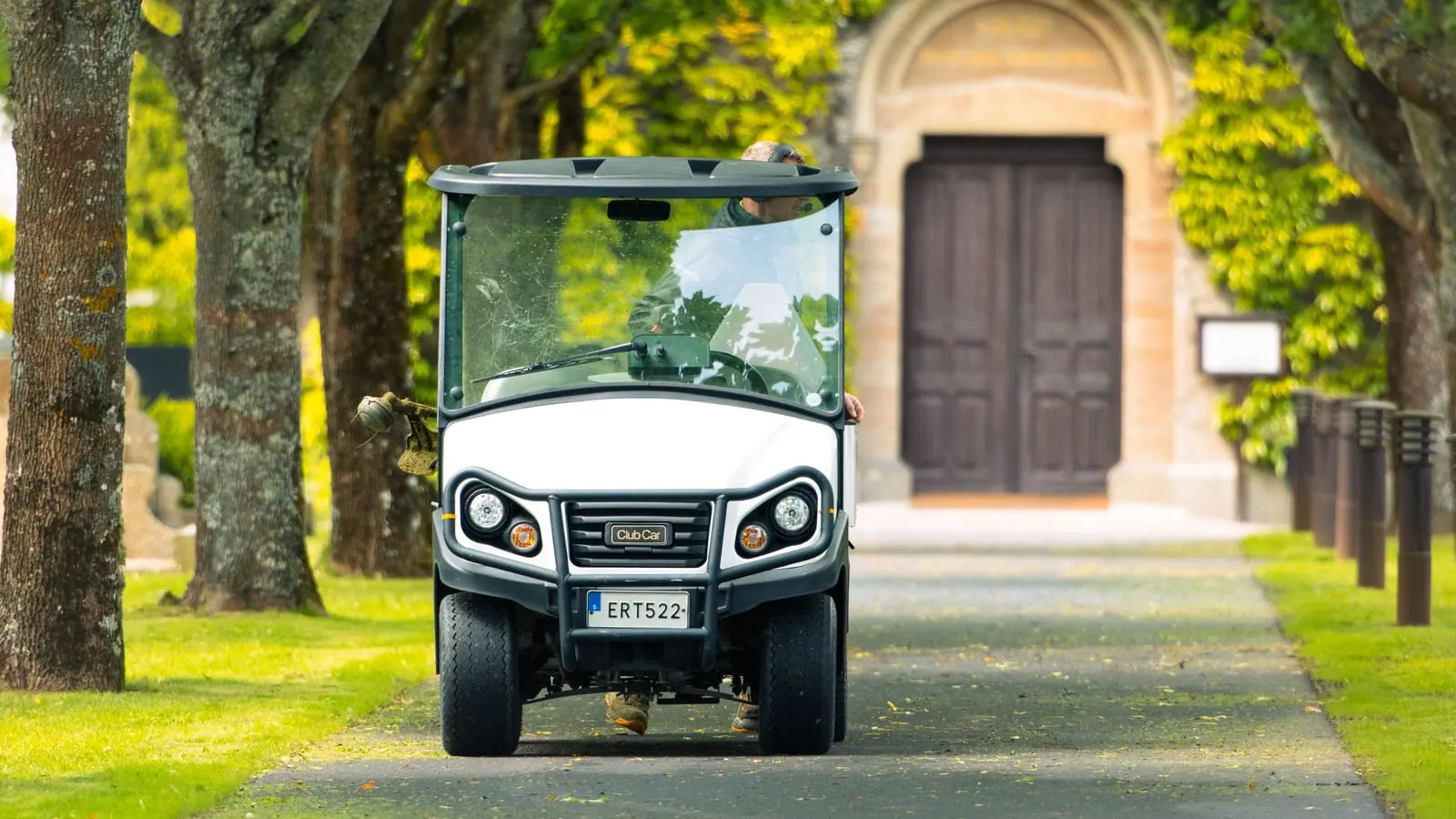 A registered street legal golf cart with a visible license plate driving along a tree-lined private road