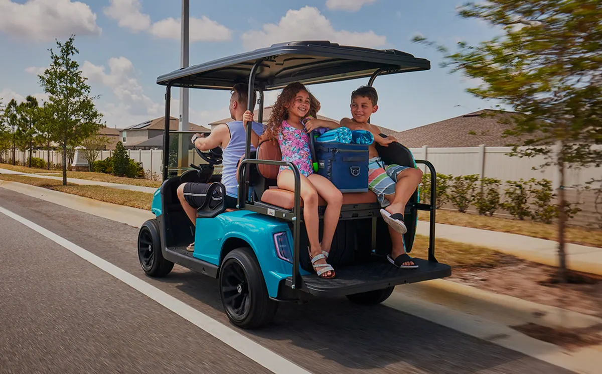 A family riding a golf cart loaded with beach gear down a neighborhood street