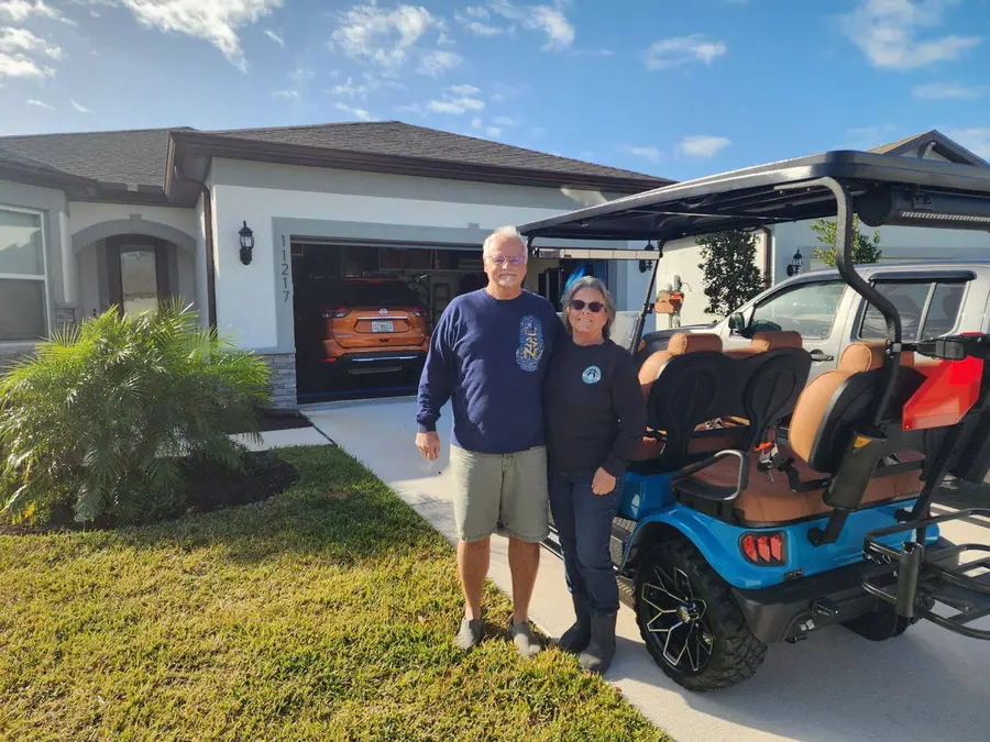Customer couple standing beside their new light blue lifted golf cart in the driveway