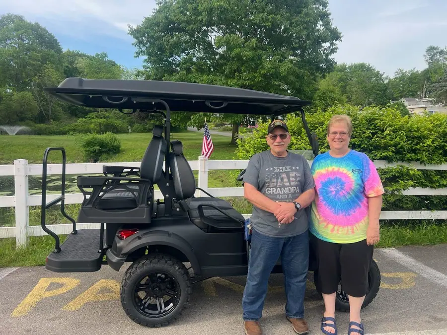 Customer couple with their new black lifted golf cart beside a pond