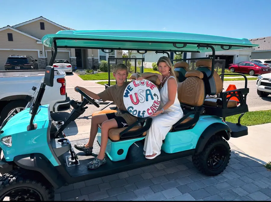 A mother and son holding a hand-painted "We Love USA Golf Carts" sign on their new cart